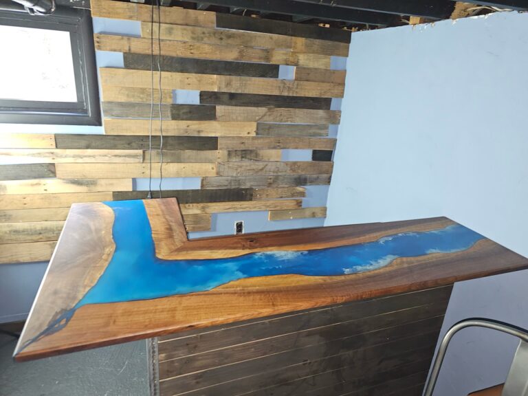 Custom Live-Edge Epoxy Bar 2 L-shaped black walnut live-edge bar top with a blue epoxy river in front of a reclaimed pallet-wood wall