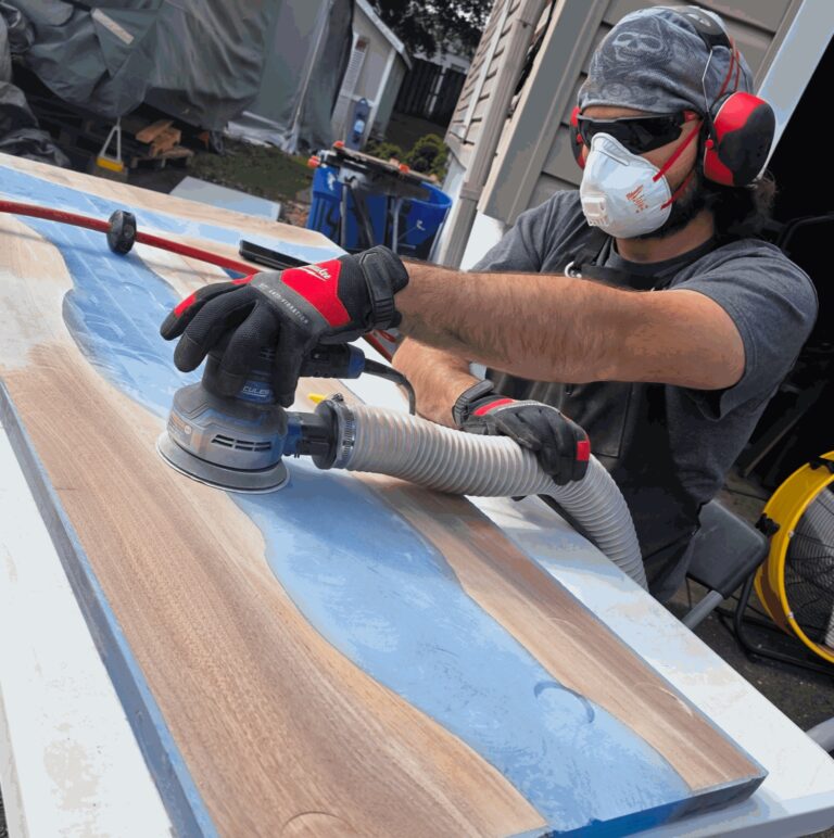 Woodworker sanding a live-edge walnut and blue epoxy slab
