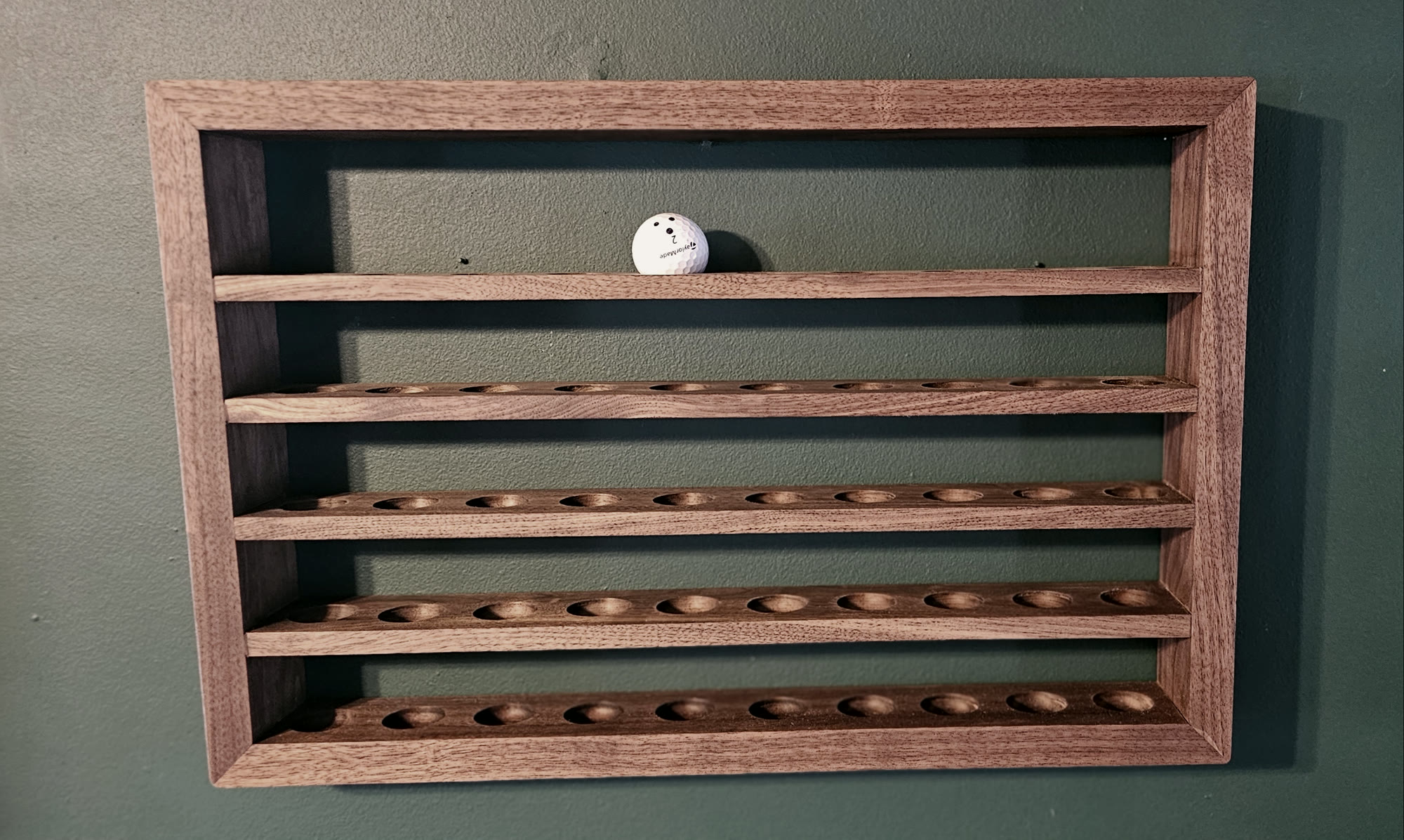 Wall-mounted black walnut display shelf with five rows of cradles for golf balls